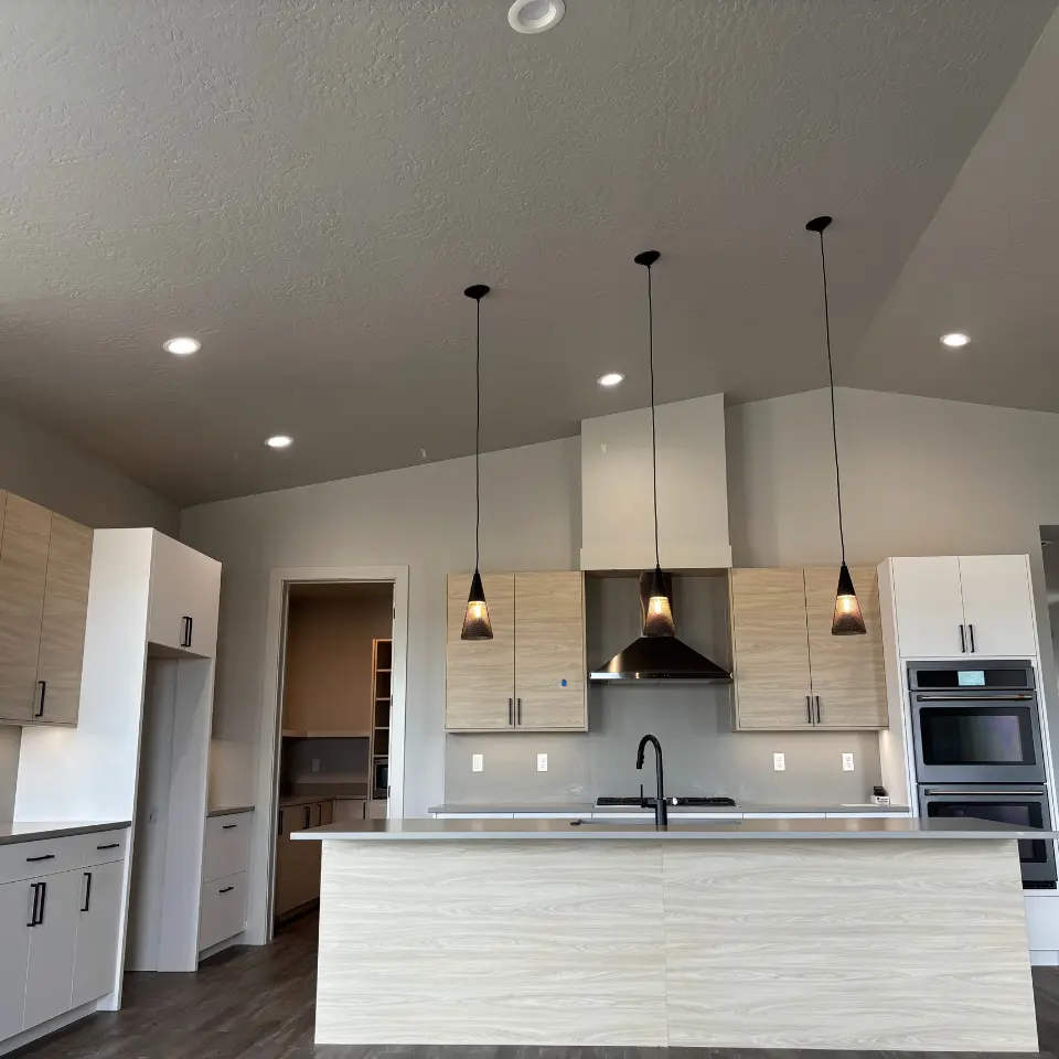 A modern kitchen featuring light wood grain cabinets, a dark kitchen island with a black faucet, and three black pendant light