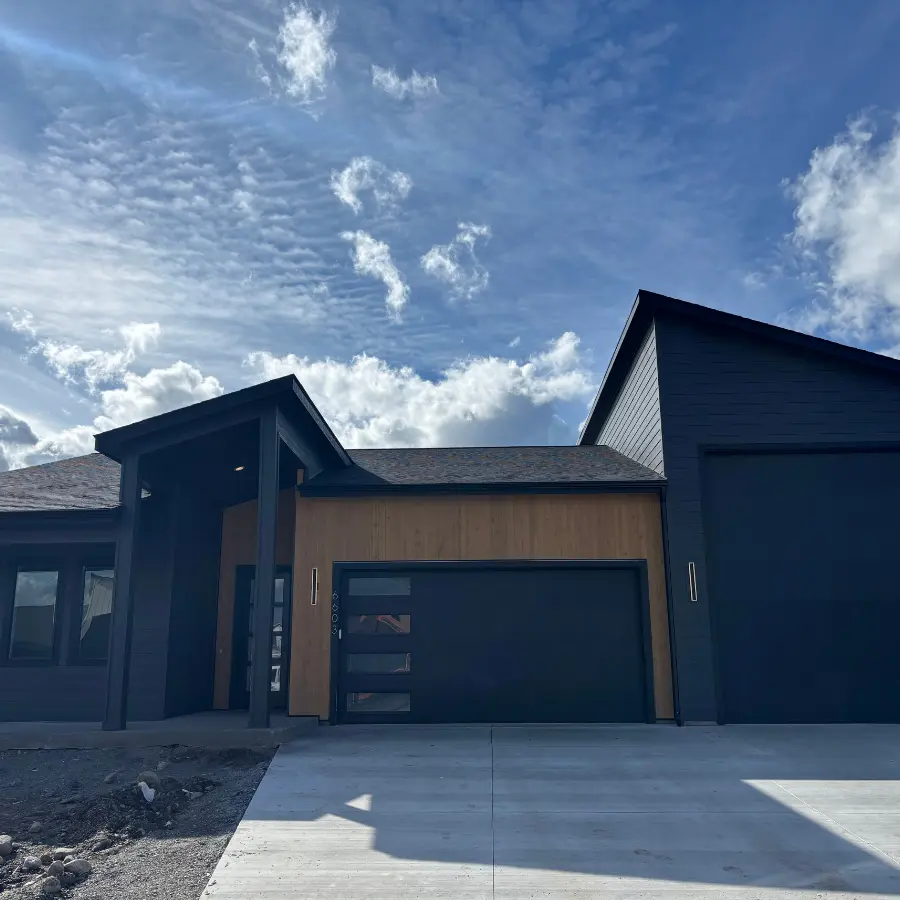 A newly built house with dark gray siding and a light wood accent wall under a blue sky with scattered clouds.