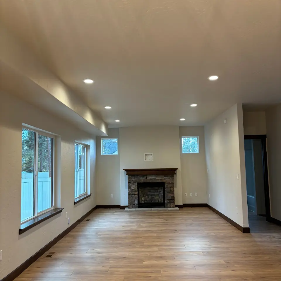 A spacious, unfurnished room with light brown wooden floors, cream colored walls, and dark brown baseboards.